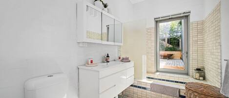 A modern bathroom with a white vanity, a large mirror, and a view of an outdoor garden through a glass door.