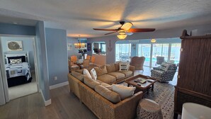 A spacious living room with a large sectional sofa, a dining area with wicker chairs, and a view of a pool through large windows. - Tranquil Waterfront Pool Home with beautiful views and sunsets and great fishing (Port Charlotte)