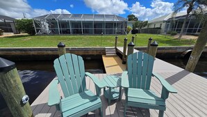 A wooden deck with two Adirondack chairs and a small table, overlooking a canal with a house in the background. - Tranquil Waterfront Pool Home with beautiful views and sunsets and great fishing (Port Charlotte)