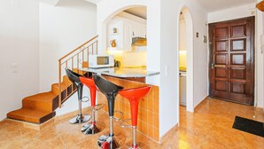 A kitchen with a microwave, a sink, and a countertop. There are three red bar stools and a wooden staircase leading to another level. - WELCS DUPLEX 025 EMP frente al Mar (Empuriabrava)
