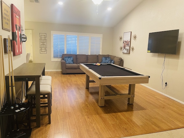 Uma sala de estar com mesa de bilhar, sofá, televisão e um espaço de jantar com cadeiras e mesa.