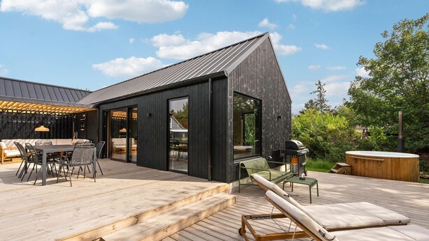 En moderne udendørs terrasse med trægulv, grillområde og en loungeseng.