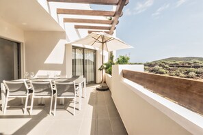 Un balcon avec une table et des chaises, une pergola en bois et une vue sur un paysage vallonné.