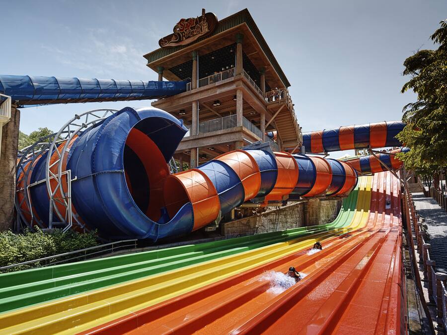 A water park with multiple water slides and a wooden building with a sign.