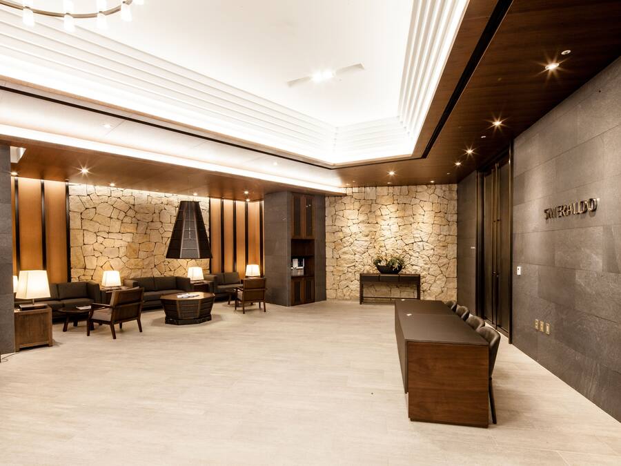 Een moderne lobby met een stenen muur, een receptiebalie en een zithoek met tafels en stoelen.
