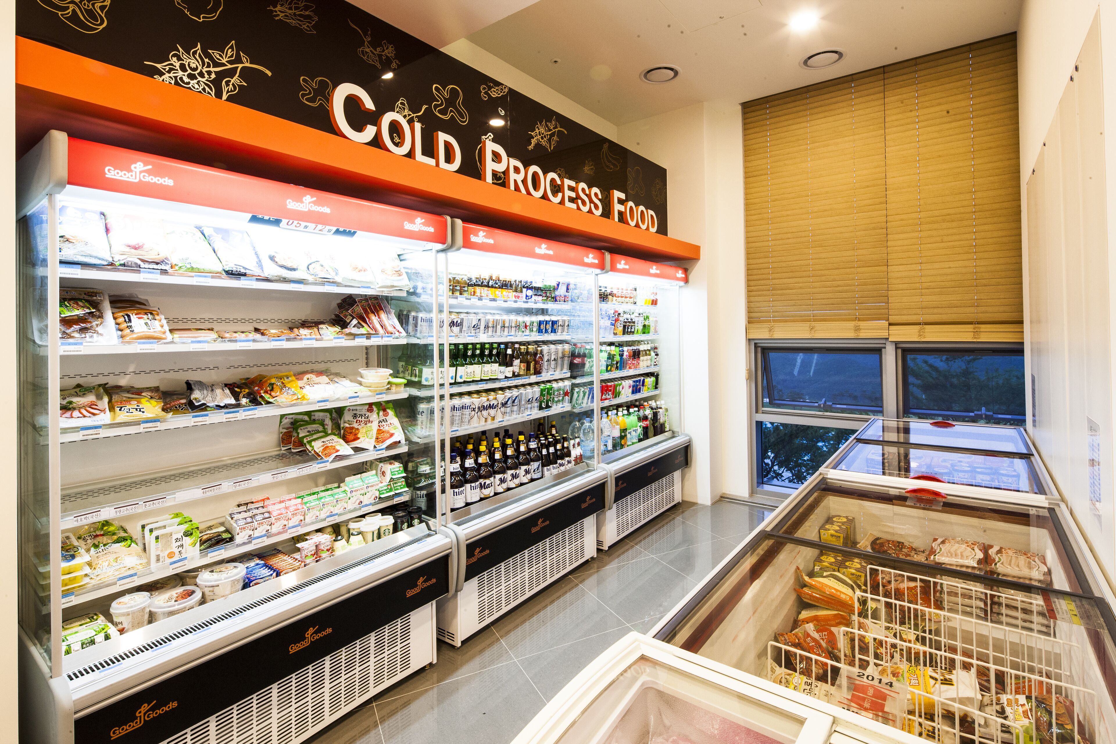 Une section réfrigérée d'un magasin, avec des étagères remplies de divers produits alimentaires et une vitrine réfrigérée contenant des produits surgelés.