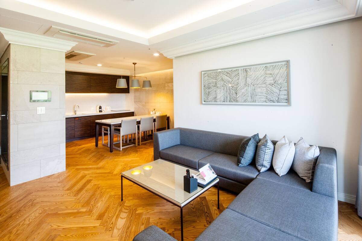 A modern living room with a grey sofa, a glass coffee table, and a wooden herringbone floor.