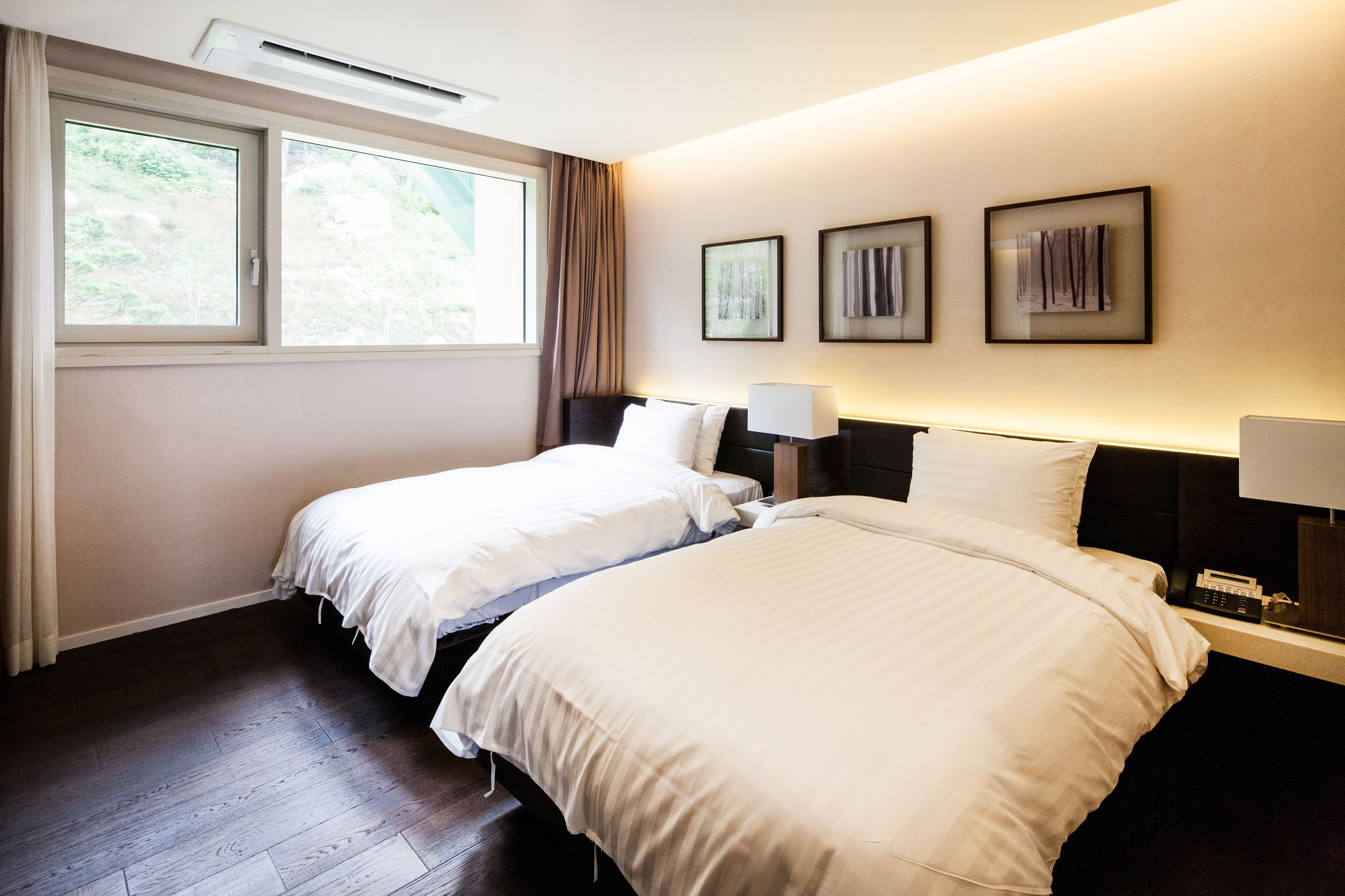 Une chambre d’hôtel avec deux lits, une grande fenêtre et trois œuvres d’art encadrées accrochées au mur.