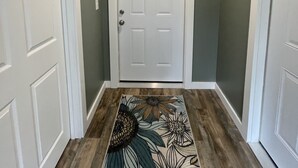 Un pasillo con una puerta blanca, un letrero de bienvenida encima y una alfombra estampada con flores en el suelo.