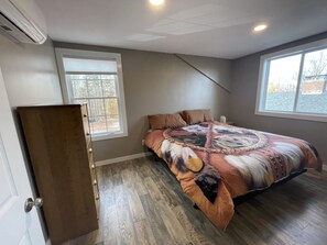 Un dormitorio con una cama grande, dos ventanas, un aparador de madera y un ventilador de techo.