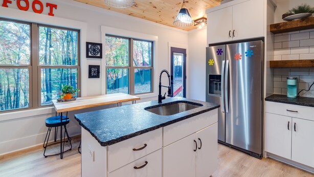 Una cocina moderna con techo de madera, refrigerador de acero inoxidable y un ventanal con vista a un bosque.