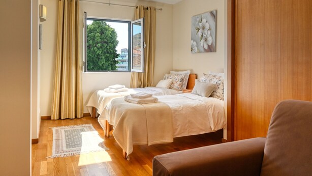 Ein Hotelzimmer mit zwei Betten, einem großen Fenster, einem Holzboden und einem Gemälde an der Wand.
