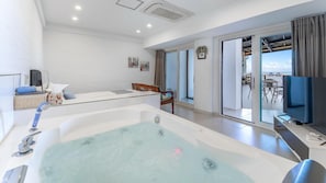 A modern living room with a large bathtub, a dining area, and a balcony with a view of the sea. - Gosung Stager (Goseong)
