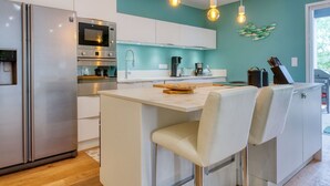 Una cucina moderna con elettrodomestici in acciaio inossidabile, un'isola centrale con sgabelli da bar e pareti color verde acqua.