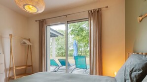 Una camera da letto con un letto grande, una sedia di legno, un tavolino e vista su una zona piscina esterna.