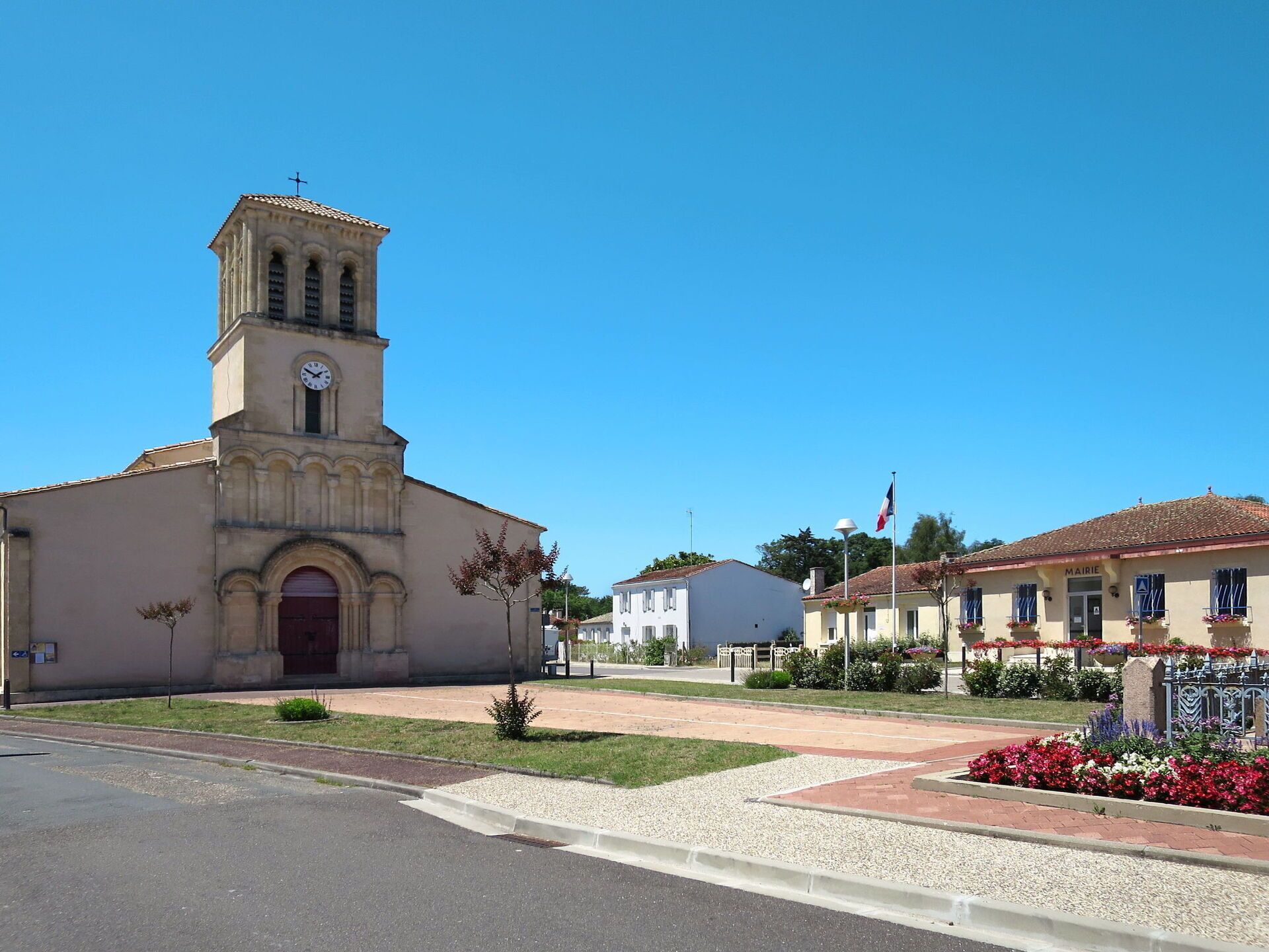 Une église dotée d’un clocher et d’une horloge, une rue avec un trottoir, et un bâtiment sur lequel on peut lire l’inscription « MAIRIE ».