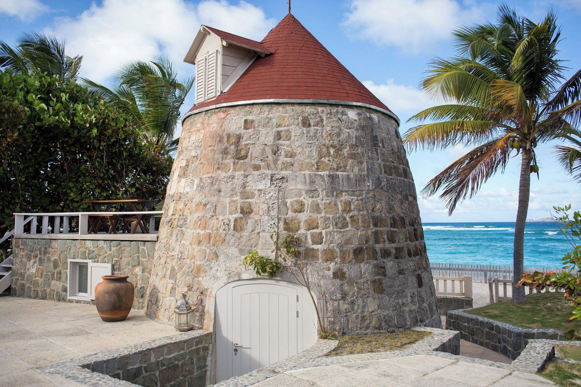 A stone tower with a red roof, a white door, and a view of the ocean.