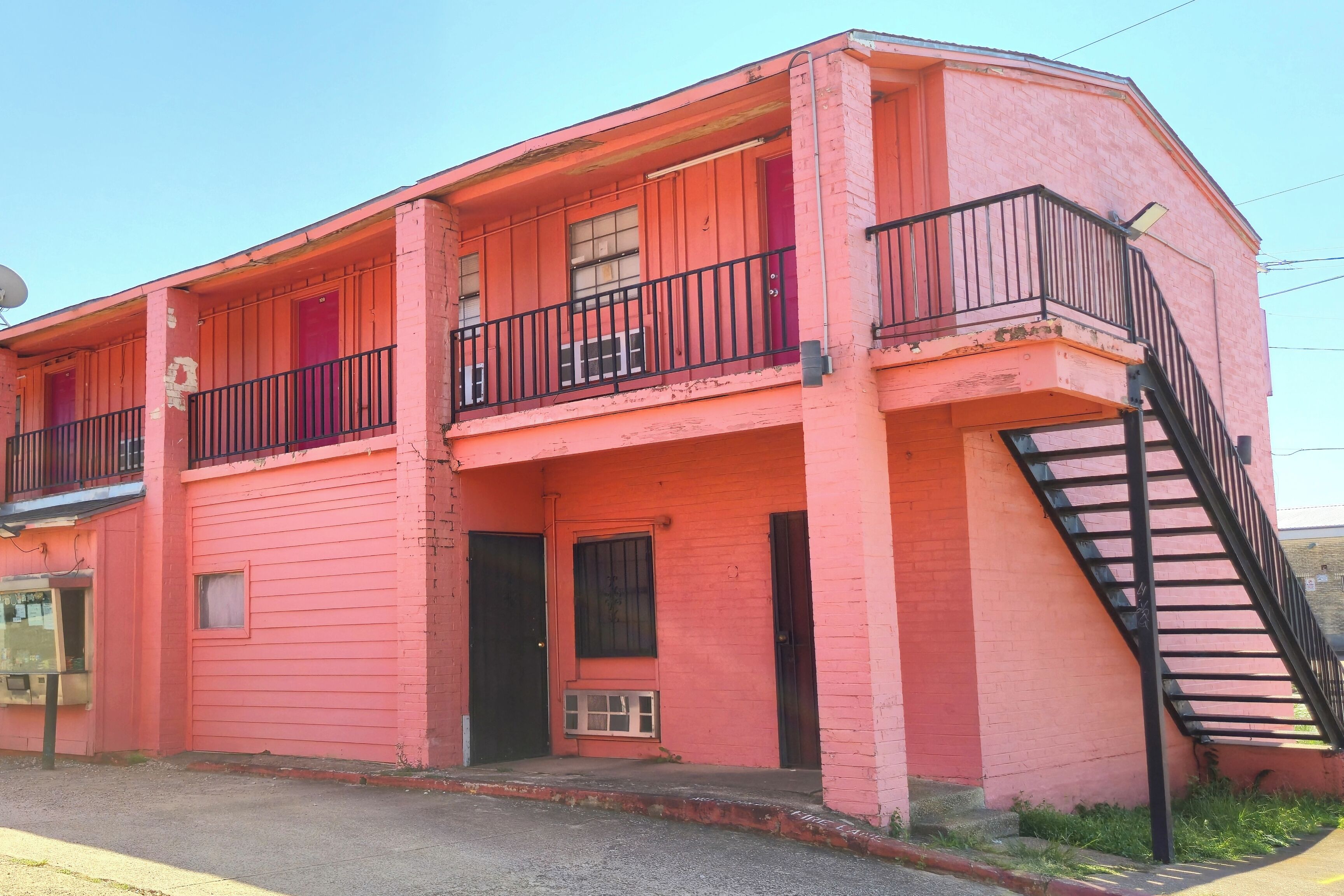 A pink two-story building with a balcony, a staircase, and a door.