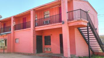 Um edifício rosa de dois andares com varanda, escadaria e porta.