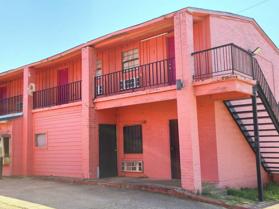 Um edifício rosa de dois andares com varanda, escadaria e porta.