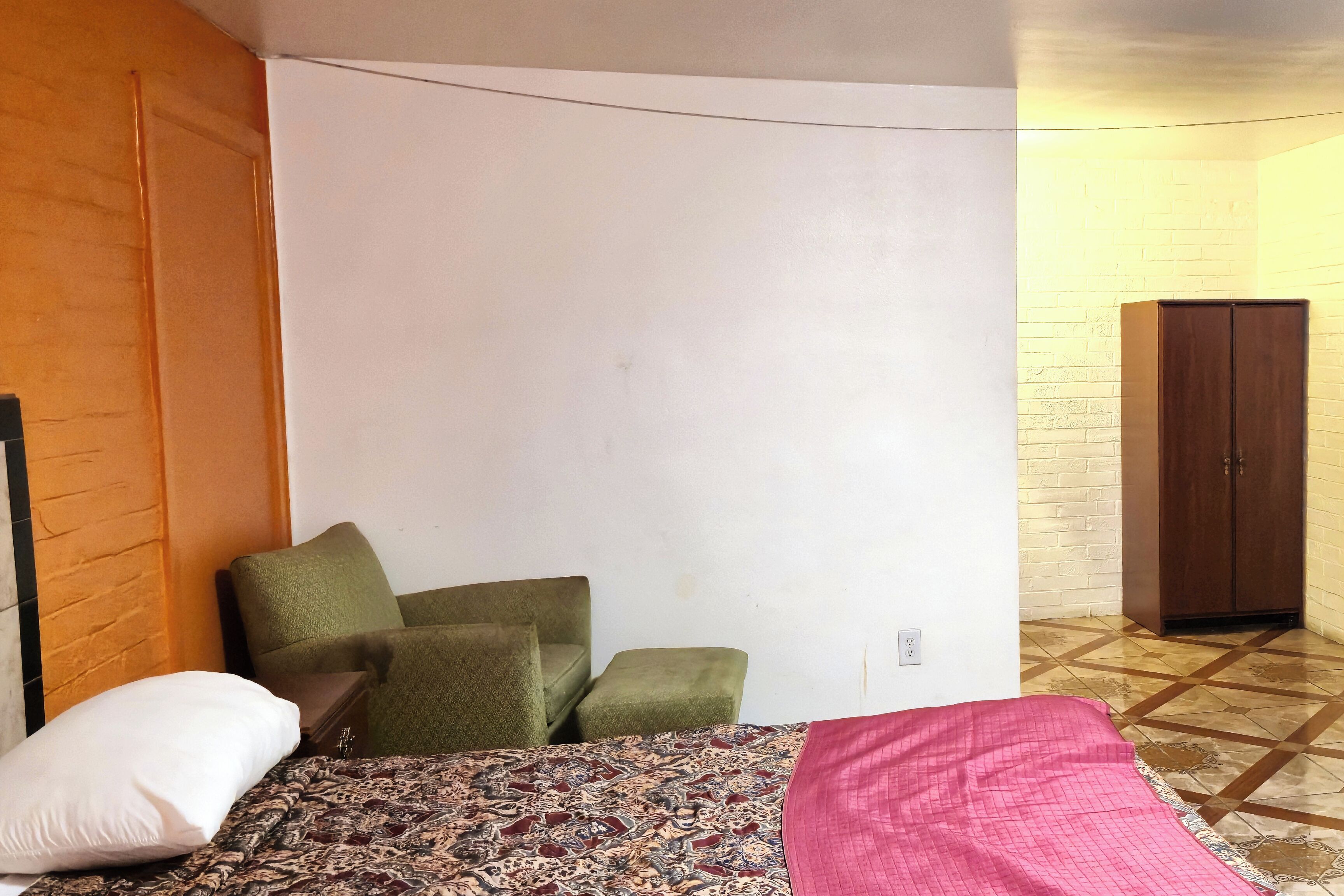 Une chambre à coucher avec un lit, des chaises vertes, une armoire en bois et une couvre-lit à motifs.