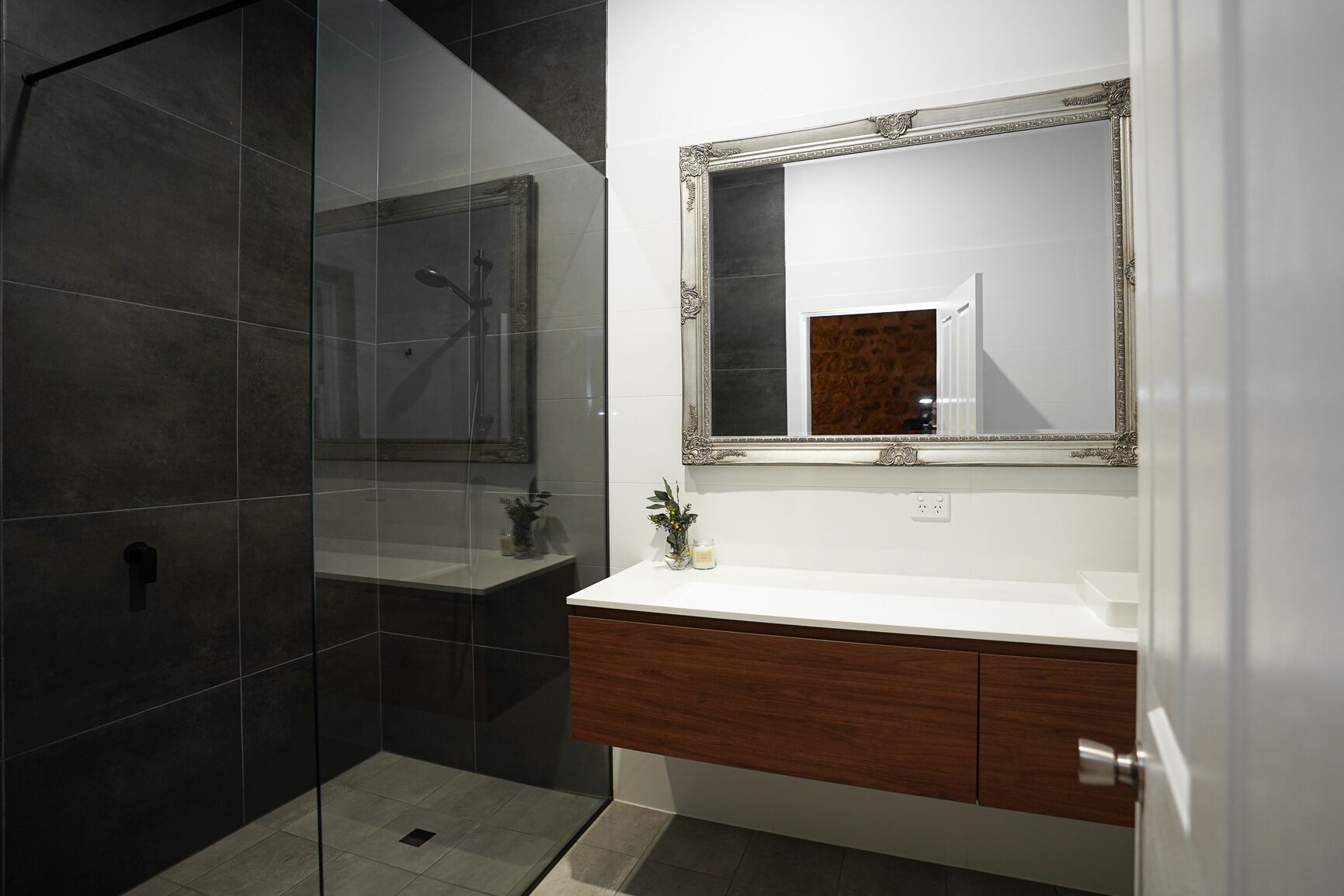 Un baño moderno con cabina de ducha de vidrio, tocador de madera y un espejo grande con marco decorativo.