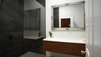 Un baño moderno con cabina de ducha de vidrio, tocador de madera y un espejo grande con marco decorativo.