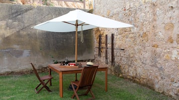 Ein Holztisch mit einem weißen Sonnenschirm, zwei Holzstühle und ein Tablett mit einer Kaffeekanne und Tassen.