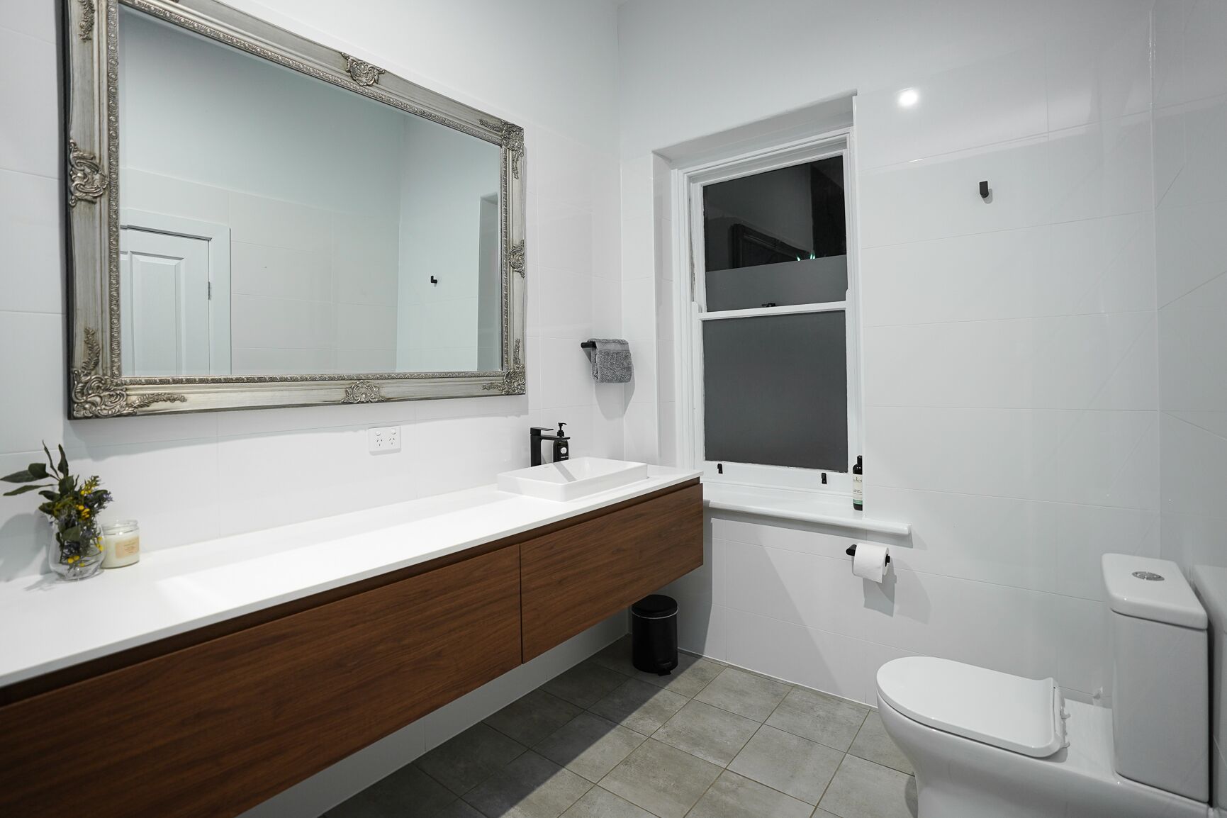 A modern bathroom with a large mirror, white sink, wooden vanity, and a toilet.