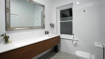 A modern bathroom with a large mirror, white sink, wooden vanity, and a toilet.