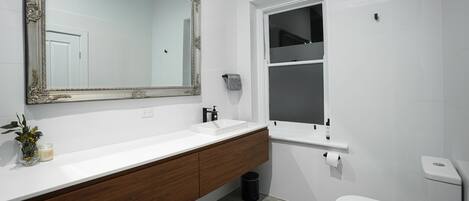 A modern bathroom with a large mirror, white sink, wooden vanity, and a toilet.