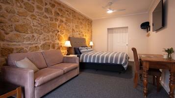 A bedroom with a stone wall, a bed with striped bedding, a sofa, a wooden table, and a ceiling fan.