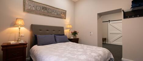 A bedroom with a large bed, two bedside tables with lamps, a wall-mounted artwork, and a sliding door closet.