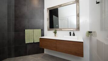 Une salle de bain avec un meuble-lavabo blanc, des murs recouverts de carreaux foncés et un grand miroir doté d’un cadre orné.