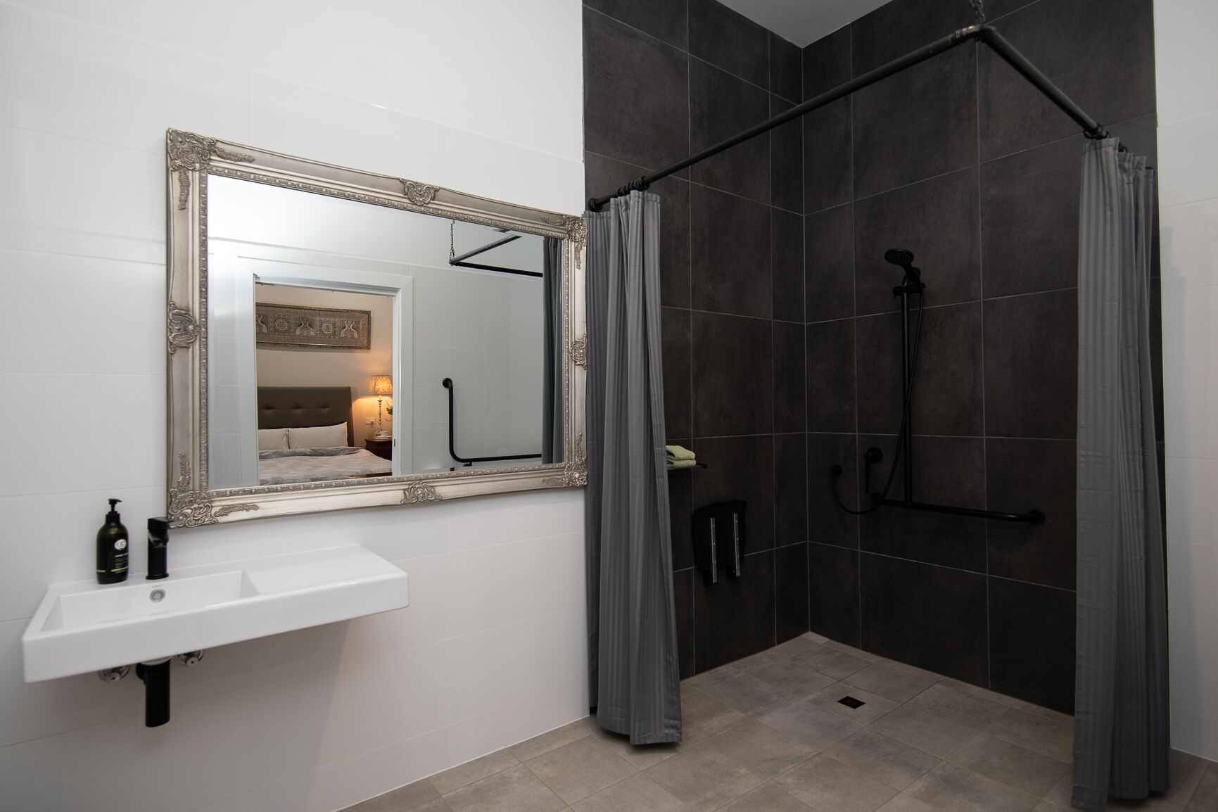 Un baño moderno con un lavamanos blanco, un espejo grande y una ducha a ras de suelo con baldosas oscuras.