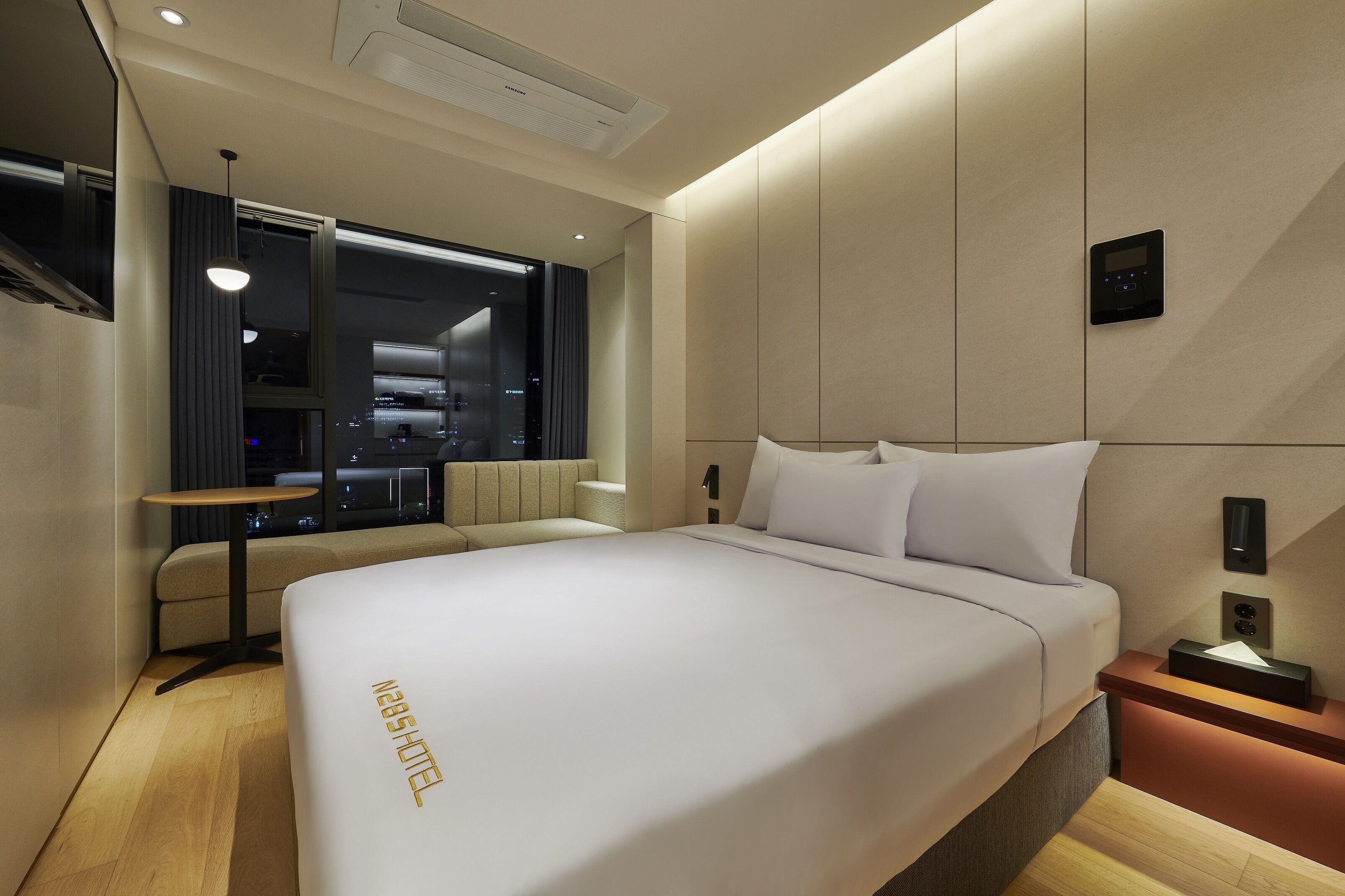 A modern hotel room with a large bed, a small table, and a view of the city at night.