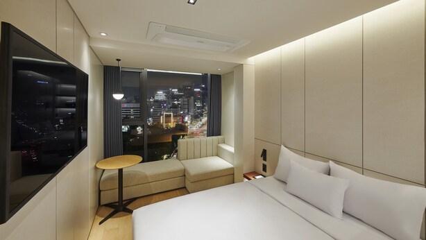 Una habitación de hotel moderna con una cama grande, zona de estar y vistas a la ciudad.