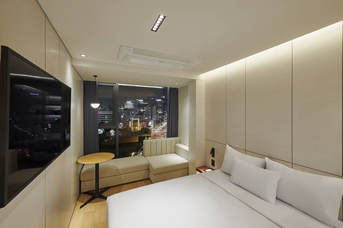 A modern hotel room with a large bed, a seating area, and a city view.