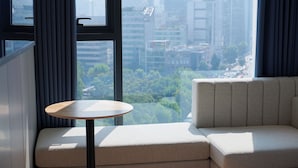 Una habitación de hotel moderna con un gran ventanal que ofrece vistas a la ciudad, una pequeña mesa redonda y un sofá.