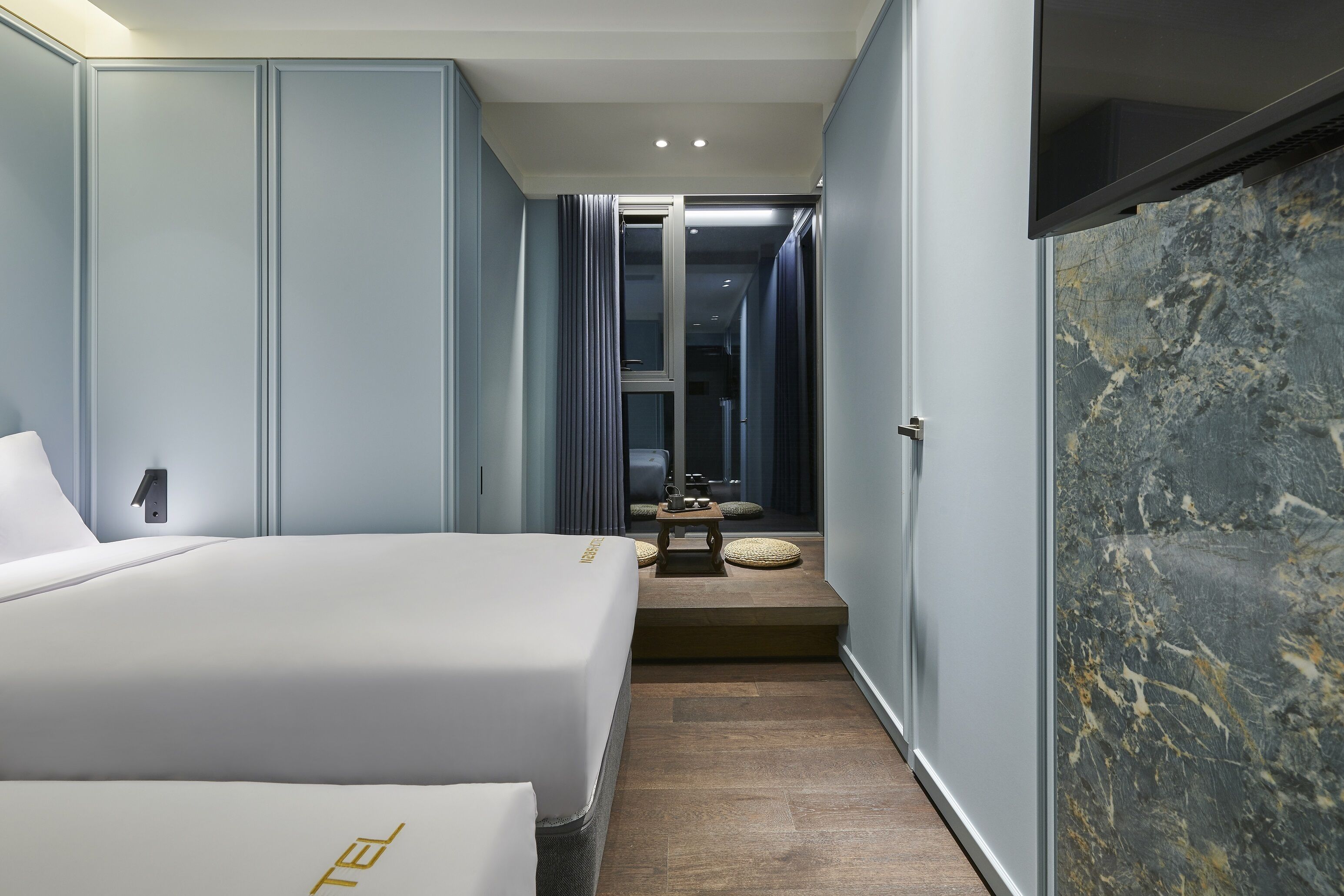 A hotel room with a bed, a small table, and a seating area with cushions.