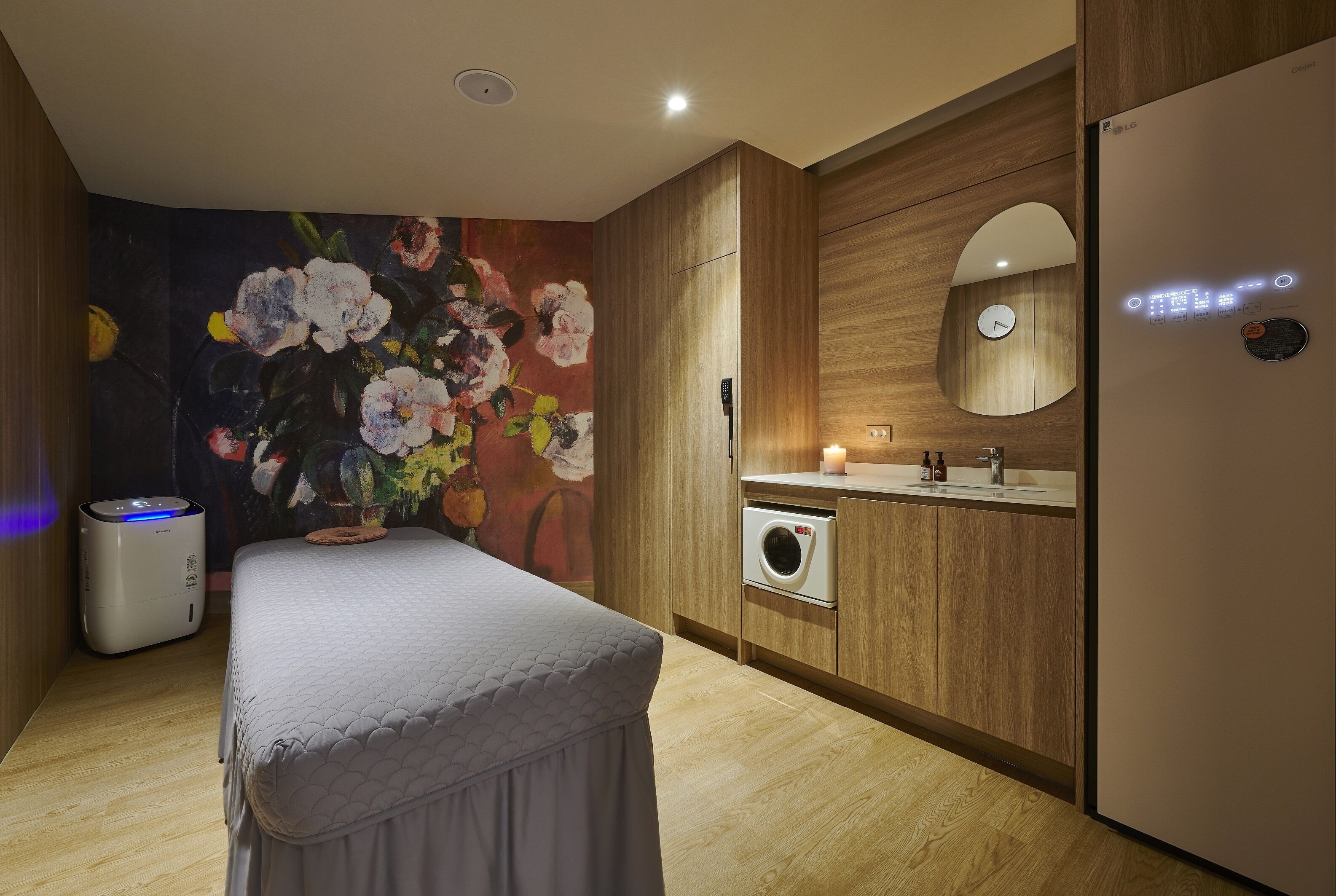 Un baño moderno con tocador de madera, lavadora integrada, cama con cubierta gris y espejo montado en la pared.