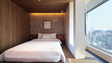 Una habitación de hotel moderna con una cama grande, techo de madera y vista a la ciudad a través de un ventanal amplio.