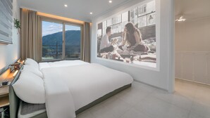 A modern hotel room with a large bed, a TV screen displaying a family, a balcony with a mountain view, and a well-lit interior. - Gapyeong Jinikidsdogchaepoolvilla (Gapyeong)