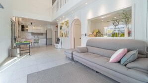 A spacious living area with a grey sofa, a small table, and a chair. There is a kitchen in the background with modern appliances and a dining area. - Gapyeong Jinikidsdogchaepoolvilla (Gapyeong)