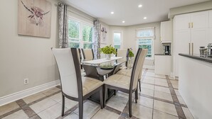 Una cocina moderna con armarios blancos, un comedor con mesa de vidrio y vistas al exterior.