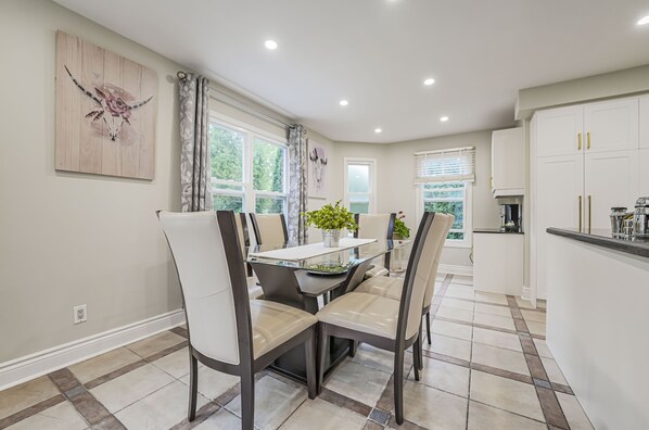 A modern kitchen with white cabinets, a dining area with a glass table, and a view of the outdoors. - Cheerful luxury 7 bedroom/7 washroom ravine house (Richmond Hill)