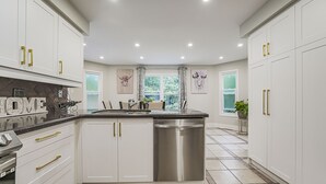 Una cocina moderna con armarios blancos, detalles dorados, lavavajillas de acero inoxidable y piso de baldosas.