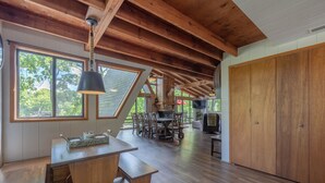 Ein geräumiges Loft mit hoher Decke, Holzbalken, einem Essbereich mit großem Tisch und Stühlen sowie einem Fernseher.