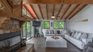 Ein geräumiges Wohnzimmer mit Kamin aus Stein, einer großen Eckcouch und einem Deckenventilator.