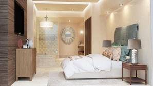 A modern bedroom with a bed, bedside tables, a TV, and a decorative mirror. - Luxury oceanfront resort suite with access to Greg Norman Signature golf course! (Cabo San Lucas)